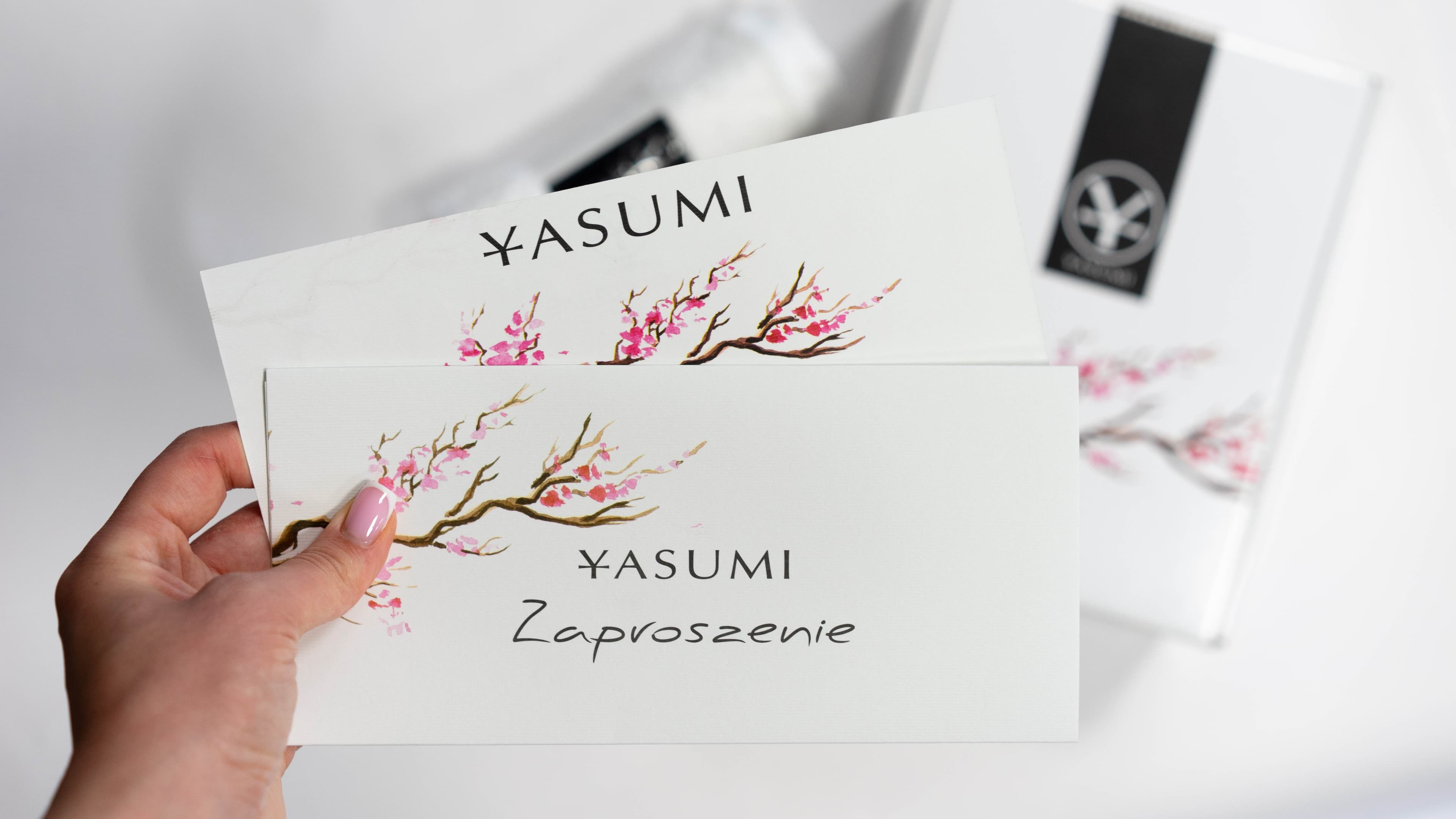 Voucher YASUMI w eleganckiej oprawie z motywem kwitnącej wiśni trzymany w dłoni